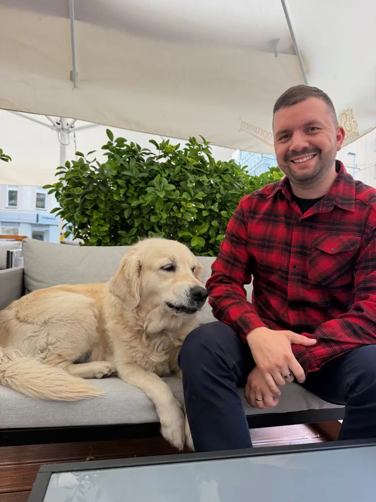 O Peter sentado na esplanada ao lado do seu retriever, com a mão nas costas do cão